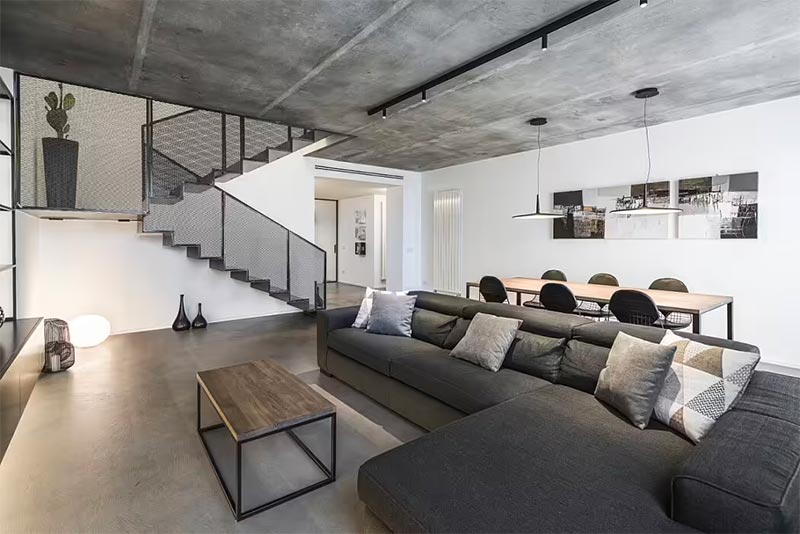 Een grote hoekbank vormt de basis van de zithoek in deze industriële woonkamer met betonnen vloer en plafond.